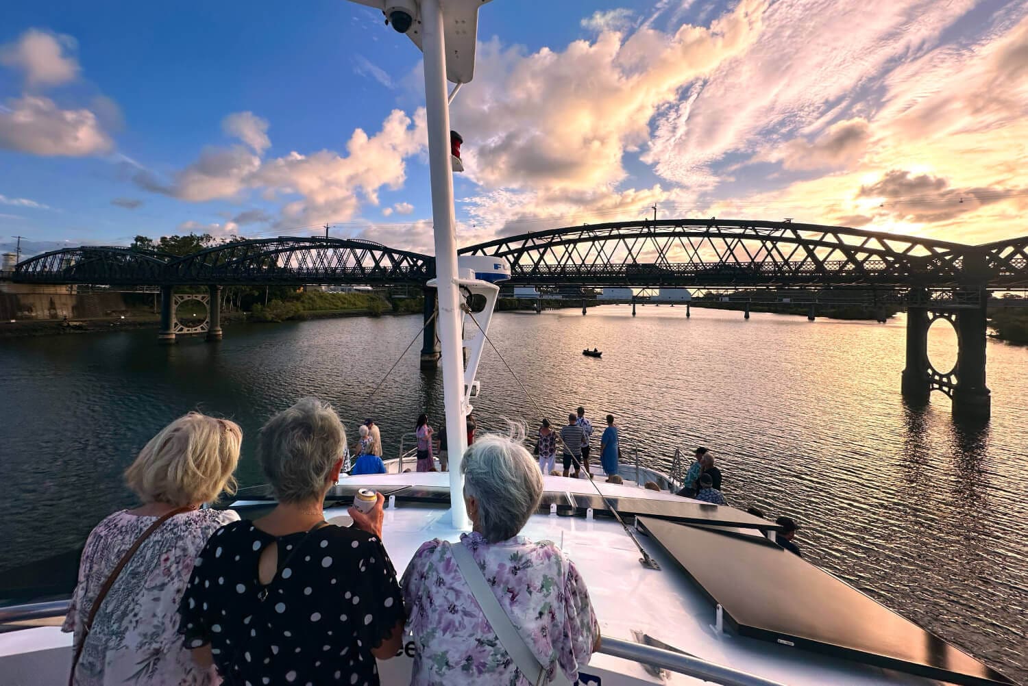 Guests on deck at sunset beneath the Burnett River bridge